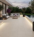 Taras z basenem, na którym ułożono beżowe płyty gresowe Marazzi Mystone Tivoli20 Beige w dużym formacie 60x120 cm, ciepła, piaskowa kolorystyka podłogi harmonizuje z nowoczesnymi meblami wypoczynkowymi i nastrojowym oświetleniem ogrodowym po zmroku