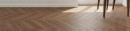 Podłoga ułożona w klasyczny wzór jodełki francuskiej chevron z płytek Marazzi Nobilis Chevron Noce Classico 11x54 cm MQ94  o głębokim, ciepłym odcieniu drewna orzechowego, całość kompozycji dopełniają białe listwy przypodłogowe