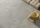 Płytka gresowa, podłogowa imitująca beton w szarym kolorze, wykończenie powierzchni matowe, Pamesa Portlandstone Gris Matt 60x120 położona na podłodze gdzie znajduje się fotel oraz jasna kanapa