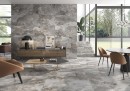Płytka gresowa, podłogowa imitująca metal w szarym kolorze, wykończenie powierzchni matowe, Pamesa Slate Way Ash Matt 30x60 położona na podłodze oraz ścianie w salonie gdzie znajduje się fotel, stół z krzesłami oraz drewniana szafka