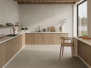 Płytka gresowa, podłogowa imitująca kamień w beżowym kolorze, wykończenie powierzchni matowe, antypoślizgowe Pamesa Sospiro Beige Antislip 60x120 położona na ścianie w kuchni gdzie znajduje się drewniana zabudowa kuchenna oraz krzesło i duże okno