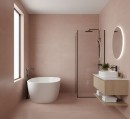 Nowoczesna łazienka wykończona matowymi, różowymi płytkami Marazzi Resin Rosa Antico 120x120 cm MQP4 imitującymi beton na ścianach i podłodze, wnętrze wyposażono w białą wannę wolnostojącą, minimalistyczną umywalkę na drewnianej szafce i czarną armaturę