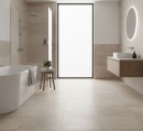 Nowoczesna łazienka wykończona wielkoformatowymi, beżowymi płytkami Marazzi Room Taupe 100x100 cm MP6H o teksturze kamienia, które pokrywają zarówno podłogę, jak i ściany, w jasnym, minimalistycznym wnętrzu znajduje się wolnostojąca wanna