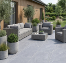 Przytulny taras z szarymi meblami wypoczynkowymi, donicami, wyjściem na ogród i jasnoszarymi płytkami podłogowymi imitującymi kamień Caesar Portraits Versilia