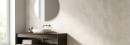 Płytka ścienna imitująca beton w beżowym odcieniu, wykończenie powierzchni matowe, Pamesa Eleganza Beige Matt 33,3x100 położona na ścianie w łazience gdzie znajduje się drewniana szafka z umywalką oraz wiszące lustro