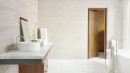 Płytka ścienna, dekoracyjna w białym odcieniu, wykończenie powierzchni matowe, ryflowane, Pamesa Rlv. Silkstone Blanco Matt 30x90 położona na ścianie w jasnej łazience z wanną oraz drewnianymi drzwiami