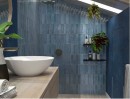 Nastrojowa łazienka z płytkami Idea Ceramica Art Nouveau Blue 25x60. Niebieska, lamelowana glazura w połysku tworzy klimat oceanicznego SPA. Głęboki błękit ścian idealnie kontrastuje z drewnianą szafką i bielą ceramiki na poddaszu.