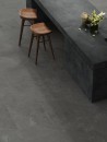 Jadalnia z wyspą kuchenną z grafitowego kamienia oraz szarymi płytkami podłogowymi imitującymi kamień na Caesar Slab2 Iron