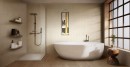 Nowoczesna łazienka wykończona jest beżowymi płytkami ściennymi Marazzi Room Wall Taupe 30x90 cm (MP66), które efektownie imitują strukturę kamienia, aranżację dopełnia wolnostojąca wanna na tle pionowo prążkowanej tekstury oraz drewniana podłoga