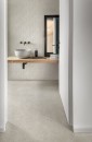 Jasna, nowoczesna łazienka została wykończona ściennymi płytkami Marazzi Room Wall Bianco 30x90 cm MP67, które subtelnie imitują naturalny kamień, minimalistyczną aranżację uzupełnia nablatowa umywalka na drewnianym blacie