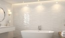 Płytka ścienna w białym odcieniu, wykończenie powierzchni strukturalne w połysku, Pamesa Mylo Rlv. Blanco Brillo 36x80 położona na ścianie w jasnej łazience gdzie znajduje się wanna, okrągłe lustro