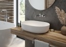 Łazienka z szarymi betonowymi płytkami, okrągłym lustrem, białą wanną wolnostojącą, drewnianym blatem oraz białą nablatową umywalką Oltens Hamnes