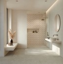 Jasna, nowoczesna łazienka wykończona szarymi płytkami Marazzi Room Wall Grigio 20x60 cm MQ7C o subtelnej strukturze kamienia, minimalistyczne wnętrze dopełnia biała umywalka nablatowa, okrągłe lustro oraz złota armatura podtynkowa