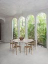 Jasna jadalnia z podłogą wyłożoną płytkami Marazzi Slow Cold Gesso 60x60 cm MPEG, które tworzą jednolitą powierzchnię dzięki dopasowanej spoinie, wnętrze z wysokimi, łukowymi oknami wychodzącymi na zieleń wyposażono w okrągły, kamienny stół