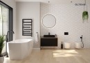 Oltens Stygg designerska wanna wolnostojąca 160x73 cm owalna wykonana z akrylu wykończona w białym połysku 12005000 wanna zamontowana w jasnej łazience z drewnopodobną podłogą, przy ścianie stoi czarna szafka z umywalką