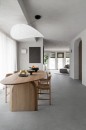 Nowoczesny salon z jadalnią, w którym szare płytki Marazzi Slow Cold Cemento R10 60x60 cm MPER imitujące beton tworzą spójną i elegancką podłogę, wnętrze uzupełnia duży drewniany stół z krzesłami oraz designerska biała lampa