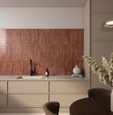 Płytka ścienna, cegiełka w brązowym odcieniu, wykończenie powierzchni w połysku, Bestile Makalu Grana 5x50 położona na ścianie w kuchni gdzie znajdują się beżowe meble oraz brązowe fotele