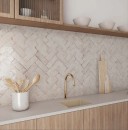 Płytka ścienna, cegiełka w białym kolorze, wykończenie powierzchni rustykalne w połysku, Bestile Musa Blanco Polished 6,5x20 położona na ścianie w kuchni gdzie znajdują się drewniane meble kuchenne wraz z zlewozmywakiem