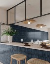 Płytka ścienna, dekoracyjna w niebieskim kolorze, wykończenie powierzchni w połysku, Gayafores Deco Artis Plus Navy 32x62,5 położona w nowoczesnym wnętrzu z barem, jasnym blatem oraz drewnianymi stolikami
