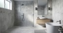 Płytka gresowa, podłogowa imitująca beton w szarym kolorze, wykończenie powierzchni matowe, Sintesi Paint White Rect. 60x119,8 położona na podłodze oraz ścianie w łazience gdzie znajduje się wanna, drewniana szafka z umywalką oraz duże wiszące lustro