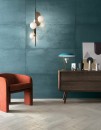 Nowoczesny salon z płytką Mirage Lemmy Indio LY 07 60x120 na ścianie. Morska, metaliczna barwa tła idealnie współgra z rudym fotelem i drewnianą komodą. Całość dopełnia designerska lampa, tworząc eleganckie, artystyczne wnętrze w stylu vintage.