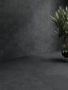 Gresowa grafitowa płytka Caesar Slab2 Dark imitująca kamień wyłożona na ścianach i podłodze. W rogu pokoju ozdobna roślina w ciemnej donicy