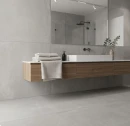 Nowoczesna łazienka z wielkoformatowymi gresami Marazzi Slow Cold Cromo 75x150 cm MPDX na podłodze i ścianach. Szare płytki o strukturze betonu tworzą tło dla podwieszanej dębowej szafki z białą umywalką, ręcznikami i czarną baterią