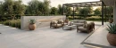 Nowoczesny taras wyłożony wielkoformatowymi, szarymi płytkami gresowymi Marazzi Slow Cold20 Nebbia 60x120 o grubości 20 mm (MPZR). Płytki imitujące beton tworzą minimalistyczną podłogę dla zestawu wypoczynkowego, ogniska i donic z agawami.