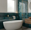 Elegancka łazienka z płytkami Marazzi Lume Blue Lux 10x10. Błyszcząca, morska ceramika na ścianach efektownie kontrastuje z białą wolnostojącą wanną, złotą armaturą oraz drewnianymi meblami, tworząc luksusowe wnętrze o rzemieślniczym charakterze.