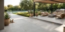 Nowoczesny taras wyłożony szarymi, wielkoformatowymi płytkami gresowymi Marazzi Slow Cold20 Cromo 60x120 o grubości 20 mm (MPZS). Płytki imitujące beton tworzą minimalistyczną podłogę dla zestawu wypoczynkowego, ogniska i donic w otoczeniu ogrodu i basenu