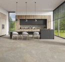 Gres Itiles La Piase Nature Naturale 60x120 w nowoczesnej kuchni z jadalnią. Szara, kamienna podłoga doskonale współgra z drewnianą zabudową, czarnymi frontami wyspy i długim stołem. Przeszklone ściany otwierają wnętrze na ogród.