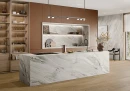 Gres Graniti Sequoia White 60x120 zdobi wyspę kuchenną oraz wnękę nad blatem. Wyraziste, szare użylenie na jasnym tle tworzy luksusowy kontrast z brązową zabudową i drewnianą podłogą. Nowoczesna, otwarta kuchnia o unikalnym, naturalnym charakterze.