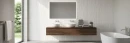 Nowoczesna łazienka ze ścianą wyłożoną płytkami Marazzi Slow Wall 3D Dash Gesso 40x120 cm MPCE. Widoczna drewniana szafka z dwiema umywalkami, podświetlane lustro, wolnostojąca wanna, okno tarasowe i złoty wieszak z ręcznikiem.