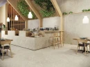 Płytka gresowa podłogowa imitująca lastryko w beżowym odcieniu, wykończenie powierzchni matowe, Baldocer Volcano Avorio Matt 120x120 położona na podłodze oraz ścianie w w pomieszczeniu gdzie znajdują się drewniane krzesła oraz wiszące lampy