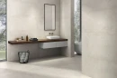 Gres Emigres America Beige 80x80 na ścianach i podłodze nowoczesnej łazienki. Ciepłe, betonopodobne płyty tworzą minimalistyczną bazę dla drewnianego blatu z umywalką nablatową. Duże okno i jasna kolorystyka nadają wnętrzu charakter.