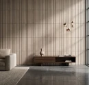 Salon z płytkami Marazzi ArtCraft Argilla Struttura 3D Bande 20x20 cm MGUS. Beżowa ściana o pionowej, prążkowanej strukturze tworzy tło dla ciemnej szafki RTV. Nowoczesne wnętrze z dużą ilością światła dziennego i betonową podłogą.