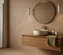 Łazienka z płytkami Marazzi ArtCraft Coccio 21x18,2 cm MGSY. Beżowe, heksagonalne kafle o matowej, surowej strukturze zdobią ścianę i podłogę, tworząc ciepłe tło dla drewnianej szafki, okrągłego lustra oraz nowoczesnej umywalki nablatowej.