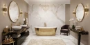 Gres Prime Ceramics Athena Carving Lappato 60x120 w luksusowym pokoju kąpielowym. Marmurowe płyty na podłodze i ścianie głównej tworzą bazę dla złotej wanny oraz czarnych blatów. Kryształowy żyrandol i okrągłe lustra podkreślają wyrafinowany styl glamour.