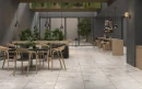 Przestronne wnętrze restauracji wykończone gresem Prime Ceramics Festive Silver Carving 60x60. Srebrzysta podłoga o wyglądzie betonu świetnie komponuje się z roślinnością i ciemnymi meblami. Wytrzymałe rozwiązanie do miejsc o dużym natężeniu ruchu.