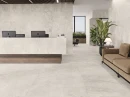 Płytka gresowa, podłogowa imitująca kamień w beżowym odcieniu, wykończenie powierzchni matowe, Baldocer Dome Bone Matt 120x120 położona na podłodze oraz ścianie w pomieszczeniu gdzie znajduje się sofa, recepcja oraz okna