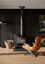 Nowoczesny salon z kominkiem wolnostojącym i designerskim fotelem, ściana wykończona czarnymi płytkami cegiełkami Marazzi Confetto Nero 5x15 cm MDSY o półmatowej powierzchni, elegancki i loftowy styl.