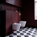 Elegancka łazienka z bordową zabudową, białą wiszącą miską wc, biały wiszący bidet, stojąca bateria bidetowa w kolorze złota szczotkowanego z kolekcji Omnires Y