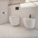 Łazienka urządzona w jasnej tonacji z białymi płytkami podłogowymi lastryko, białą wiszącą misą wc, biały wiszący bidet, stojąca bateria bidetowa w kolorze grafit szczotkowany z kolekcji Omnires Y