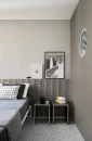 Sypialnia z szarymi płytkami 3D Marazzi Confetto Avio 3D Savoiardo 5x15 cm MEUY na ścianie za łóżkiem. Płytki mają trójwymiarowy wzór Savoiardo. Obok stoją stoliki nocne, lampa i wiszą grafiki. Na podłodze terrazzo.