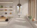 Beżowa industrialna płytka gresowa imitująca beżowy beton Saime Travertino Crosscut Beige Nat 60x60 T680108 na ścianach i podłodze salonu odzieżowego. Czarne akcenty w postaci podłużnego okrągłego lustra w czarnej ramie.