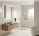 Jasna łazienka z płytkami ściennymi i podłogowymi Marazzi Terramater Vaniglia Lux 37,5x37,5 MPLX. We wnętrzu znajduje się drewniana szafka z umywalką, podświetlane lustro, kabina prysznicowa walk-in oraz wolnostojąca wanna.