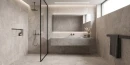 Jasno szara gresowa płytka imitująca industrialny minilalistyczny surowy beton Artistica Deep Stone White Natural 60x120 w jasnej łazience. Kabina prysznicowa typu Walk-In, Betonowy blat z umywalką oraz czarna armatura podtynkowa.