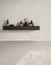 Fap Ceramiche Materia Pura Trama Bianco 60x120- strukturalna, geometryczna płytka gresowa imitująca beżowy beton o geometrycznej powierzchni na ścianie łazienki. Szara betonowa podłoga, czarna półka z odświeżaczem i kosmetykami w brązowych butelkach.