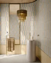 Delconca Ghiaccioli GH 1 Vaniglia Brick 6x25- beżowa, ścienna płytka cegiełka w połysku, na ścianie łazienki w połączeniu z niebiesko-szarą cegiełką. Wolnostojąca marmurowa umywalka, szara podłoga i złota armatura.