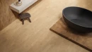 Emil Provenza W-Circles Walnut Brick Naturale 5,3x30 ENJA- gresowa płytka imitująca ciemne drewno z widocznymi słojami  na ścianie łazienki. Jaśniejsze płytki na podłodze, czarna wanna wolnostojąca na ciemnym drewnianym podeście.